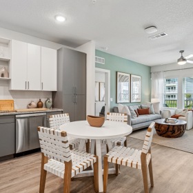 Modern open-concept apartment interior at Momentum Blanding featuring a dining area, stylish kitchen with white and gray cabinetry, and a bright living room with large windows.