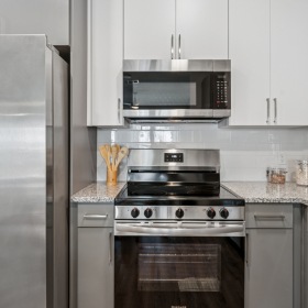 Detailed view of the kitchen at Momentum Blanding Apartments showing stainless steel refrigerator, oven, microwave, and granite countertops with jars of pasta and food items.