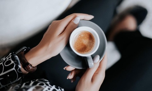 business woman sits next to a marble table with books and holds a saucer with a cup of espresso